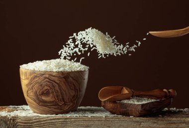 Bej arka planda stop-motion beyaz pirinç sıçraması. Pirinç, ahşap bir kaseye dökülür. Boşluğu kopyala.