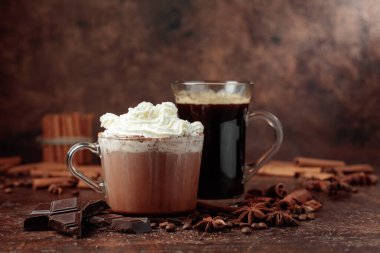 Kremalı sıcak çikolata ve sade kahve. Kahverengi bir masada malzemeli sıcak bayram içecekleri..