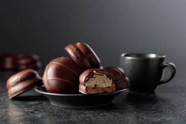 Çikolatalı tatlı ve siyah bir masada kremalı bir fincan kahve. Boşluğu kopyala.