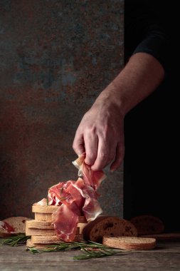 Prosciutto with bread and rosemary on an old rustic background. Traditional Mediterranean food. Copy space.