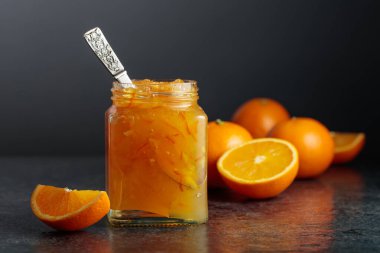 Siyah taş bir masada cam kavanozda ev yapımı portakal reçeli. Siyah arka planda çöl olan taze meyve ve kavanoz. Boşluğu kopyala.