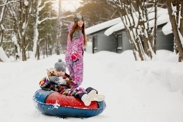 冬のエンターテイメントとレジャーのコンセプト ママは雪のチューブに乗って彼女の娘を公園のパスに沿って — ストック写真
