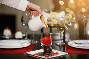 Bir kafede akşam yemeği için masa hazır. Sıcak çikolata bir sürahide kekin üzerine dökülüyor. Seçili odak.