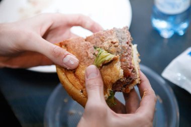 Bir kafedeki masada bir adamın elindeki hamburgeri ısırdı..