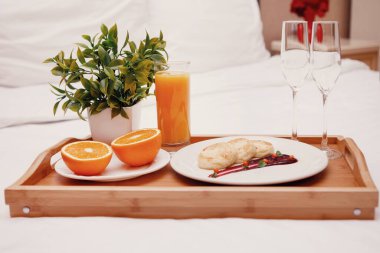 Yatakta romantik bir akşam yemeği için yemek tepsisi. Şarap bardakları, elmalar ve tabakta krepler, yeşil bitkilerle dolu bir tencere..