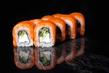 Japon somonu ve pirinç suşisi iplikli mermerden siyah bir zemin üzerinde yuvarlanıyor..