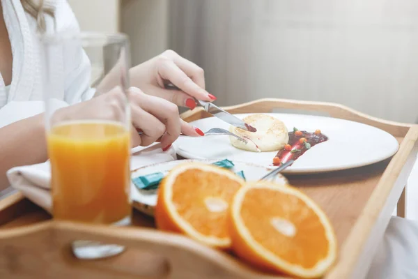 女性的手和早餐在托盘上 女孩用一把小刀 一杯橙汁和附近的两个新鲜水果 用果酱切薄饼 精选焦点 — 图库照片