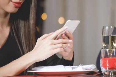 Güzel bir kadın kafedeki bir masada akıllı telefon okur..