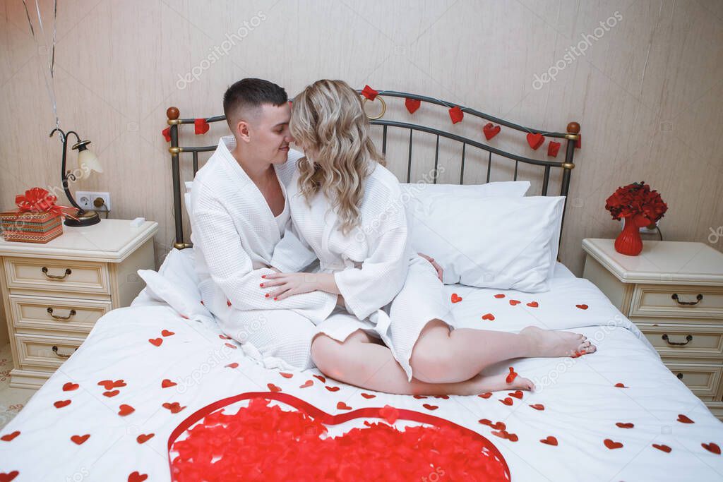 Lovers in a romantic bed. Festive interior with a red heart of rose petals. Loving couple, hugs, romance, bedroom. Valentine's Day