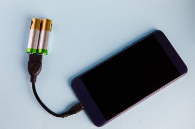 İki AA alkalin pil akıllı telefonu şarj eder. Beslenmek. Mavi arka plan. Temiz enerjinin sembolü. Çevre dostu.
