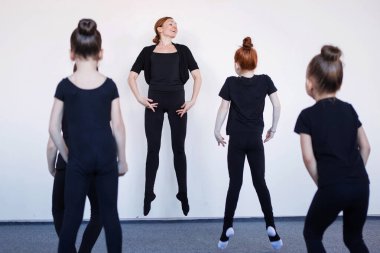 Koç, Entrechat 'ın nasıl yapıldığını gösteriyor. Dans, bale ya da ritmik jimnastik dersinde siyah tayt giyen genç kızlar..