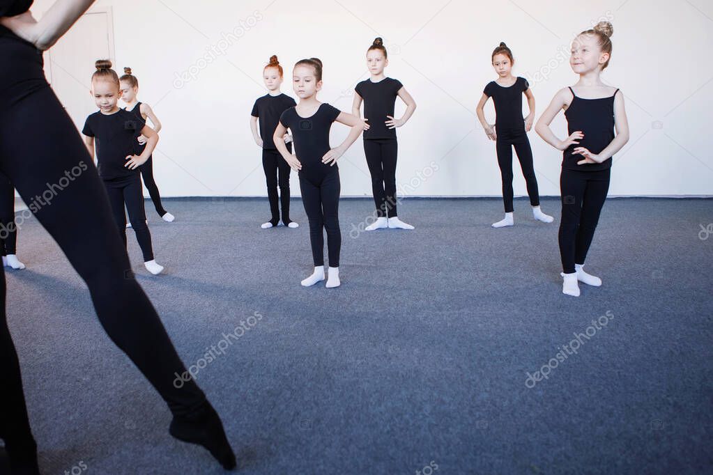 Leg trainer in the foreground. Teenage girls in black leotards in a dance, ballet or rhythmic gymnastics lesson. Selected Focus. Black leotard, hair in a bun, white socks.