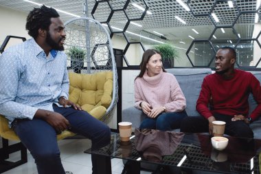 Çok uluslu erkek ve kadınların üç arkadaşından oluşan bir grup bir kafe veya restoranda iletişim kurar, gülümser ve bir masaya güler..