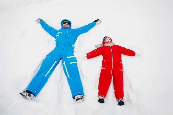 Snow Angel. Dad and son in winter red and blue clothes lie in the snow. Selective focus, blurred background.