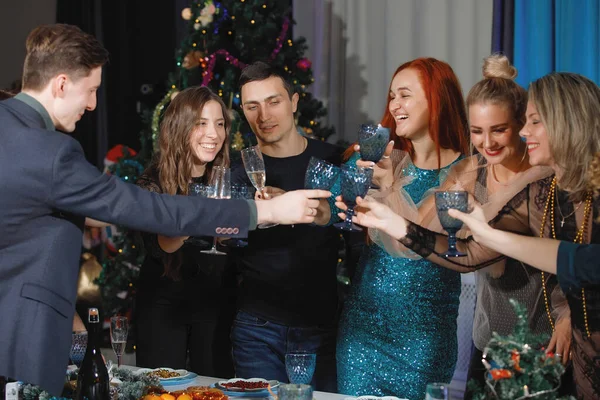 有许多朋友在圣诞树旁的餐桌旁庆祝圣诞节或新年 他们都有花环 女人笑 用香槟酒碰杯 — 图库照片