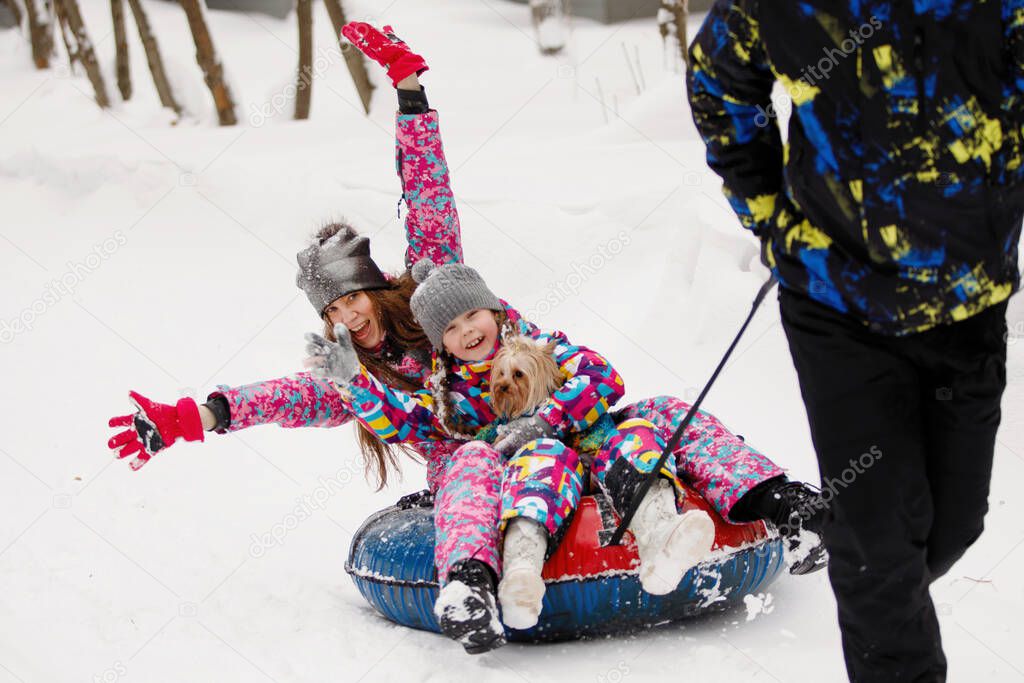 Winter entertainment and leisure concept. Daddy rides the whole family on snow tubing along the paths in the park.