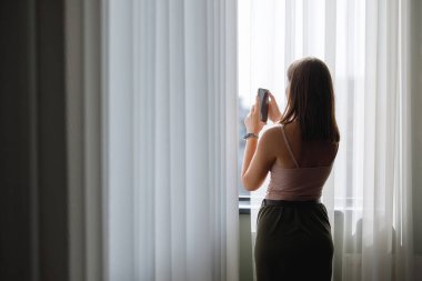 Pencereden akıllı telefondan fotoğraf çeken bir kadın..