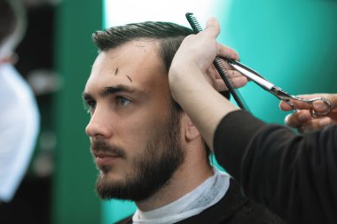 Usta kuaför salonundaki bir kuaförde sakallı bir adamı makasla keser. Seçici odak, bulanık arkaplan.