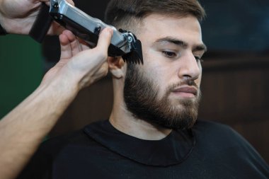 Usta berber salonundaki kuaförde saç makasıyla sakallı bir adamı kesiyor. Seçici odak, bulanık arkaplan.