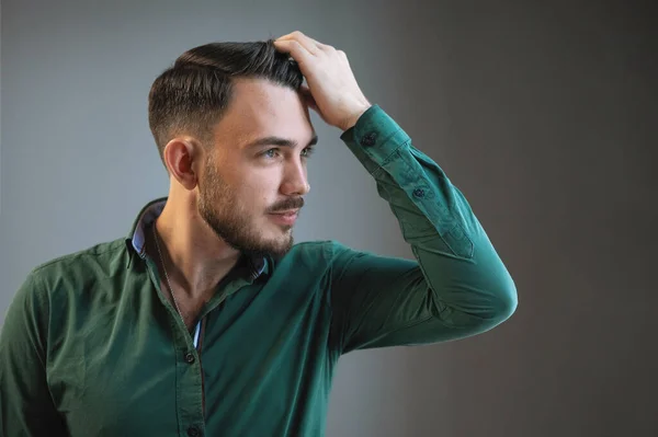 Young, handsome bearded man model poses for the camera in a green shirt, against a gray background.