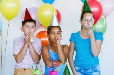 Parlak, sevimli çocuklar doğum günü kutluyor. Çokuluslu parti, balonlar, şapkalar, gülücükler ve neşe, gençler dikkatle izleyin performansı.