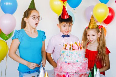 Parlak, sevimli çocuklar doğum günü kutluyor. Çok uluslu parti, balonlar, şapkalar, gülümsemeler, masanın yanında elinde pasta olan gençler..