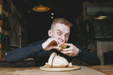 Genç sarışın adam duygusal olarak bir kafedeki masada sandviç yiyor..