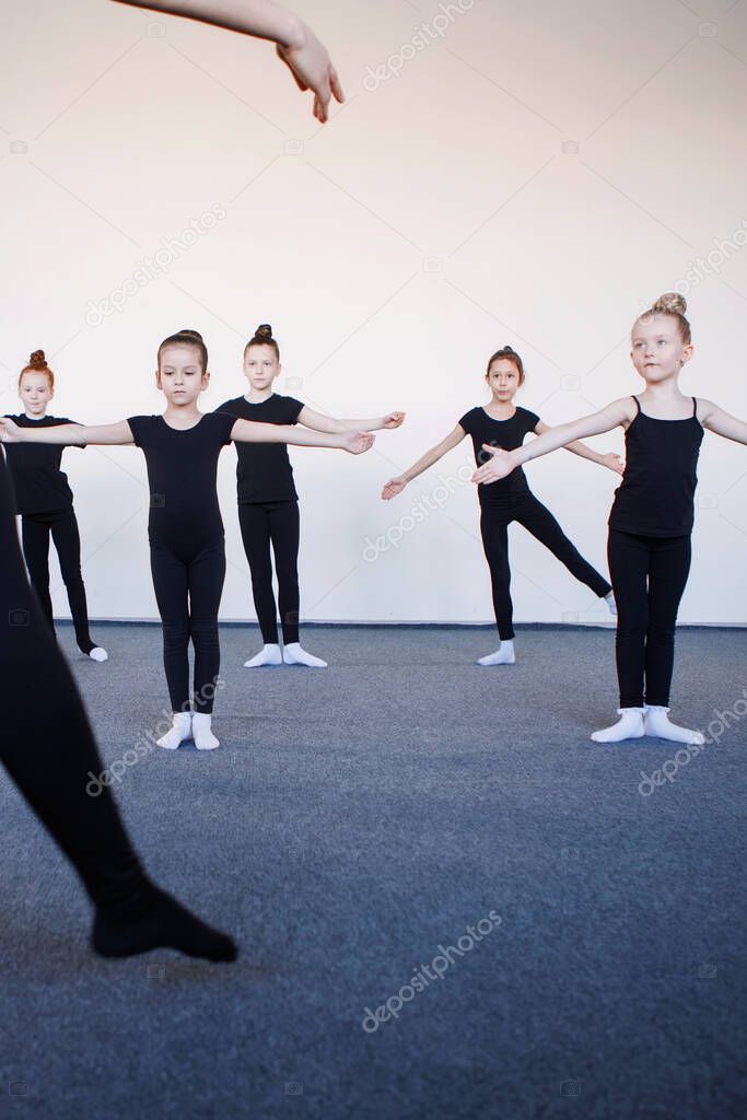 Leg trainer in the foreground. Teenage girls in black leotards in a dance, ballet or rhythmic gymnastics lesson. Selected Focus. Black leotard, hair in a bun, white socks.
