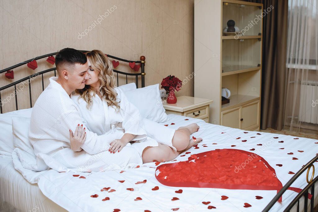 Lovers in a romantic bed. Festive interior with a red heart of rose petals. Loving couple, hugs, romance, bedroom. Valentine's Day