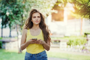 Şehir parkında sarı tişörtlü ve kot pantolonlu akıllı bir kadın..
