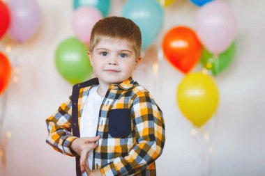Doğum günü kutlamasında ekose gömlekli mavi gözlü bir çocuğun portresi. Çok renkli balonların arkaplanı.