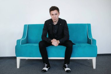 Siyah takım elbiseli, beyaz çizmeli sert adam kanepede oturuyor..