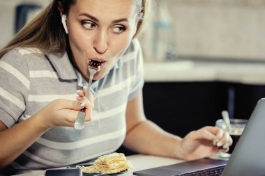 Masada dizüstü bilgisayarı ve ödevi olan bir kadın var. Mutfak içi, günlük, akıllı telefon, kablosuz kulaklık. Salgın, koronavirüs salgını.