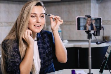 Kadın blogcu internette akıllı telefondan kaş makyajı yapıyor. Coronavirus karantina ödevi, sosyal mesafe, özel girişimci. Seçili Odaklanma.