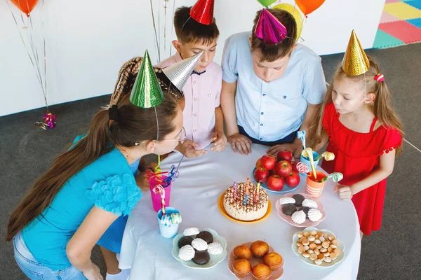 Gençler Kutlamada Şapkalar Balonlar Içinde Yuvarlak Masadaki Kekin Üzerindeki Mumları — Stok fotoğraf