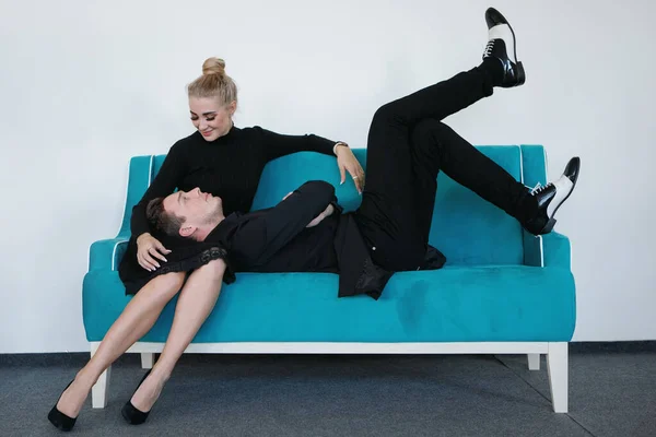 穿着黑色西装和白色靴子的酷哥躺在一个金发姑娘的膝上 坐在一个碧绿的沙发上 男人和女人在沙发上 — 图库照片