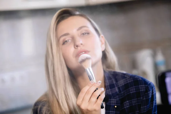 Woman shows a cosmetic brush with tonal powder.