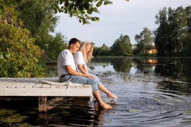 Bir çift, bir göl ya da nehrin kıyısındaki ahşap iskelede oturur.