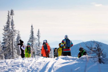 Kar yağışlı bir kış günü bir kayak merkezinde parlak renkli kıyafetli bir grup kaykaycı. Sağlıklı dinlenme kavramı. Aktif hayat. Seçici odaklanma, bulanık arkaplan. 14 / 11 / 2020 Sheregesh, Rusya