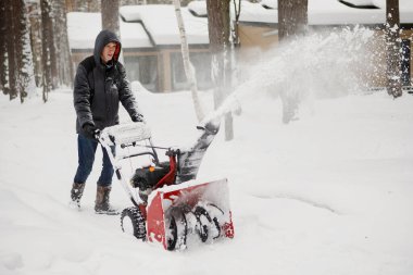 Kapüşonlu ceketli bir adam kar temizleme makinesiyle kar temizliyor..