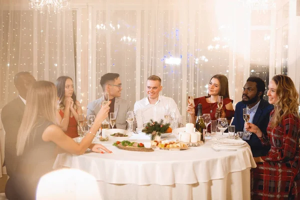 跨国公司的人坐在节日桌上 喝着香槟酒 微笑着 在餐馆里聊天 有选择的焦点 模糊的灯光 — 图库照片