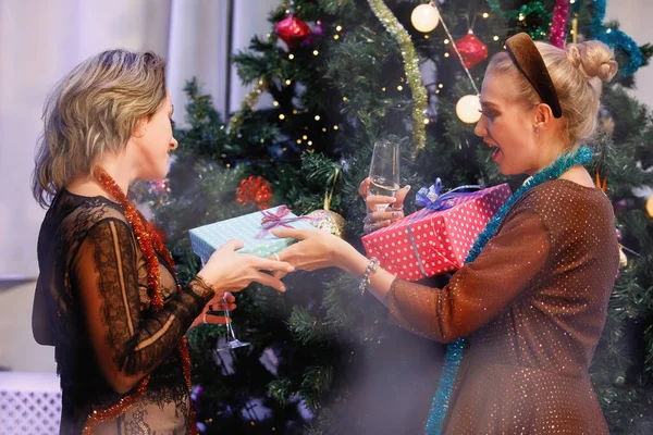 两个女朋友在一棵圣诞树旁互相赠送礼品盒 — 图库照片