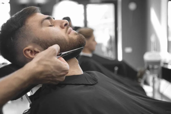 主人在理发店的理发店里用剪刀剪掉了一个人的胡子 有选择的重点 模糊的背景 — 图库照片