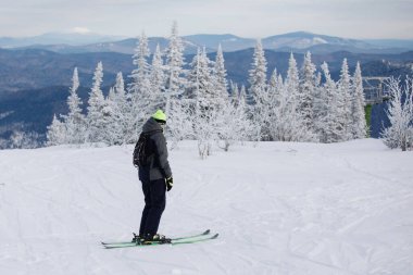 Kayakçı, doğal bir tatil köyündeki karlı bir dağın yamacında kayak yapmaktır. Kayak malzemeleri: siyah pantolon, örgü şapka, kalın ceket, gözlük. Seçici odak.