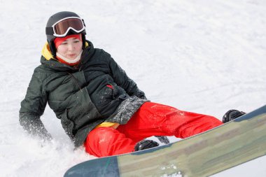 Karlı bir dağın yamacında bir kadının snowboard 'a düşüşü. Kayak ekipmanları: kırmızı pantolon, kalın ceket, şapka, doğal bir tatil köyünde güvenlik gözlükleri..