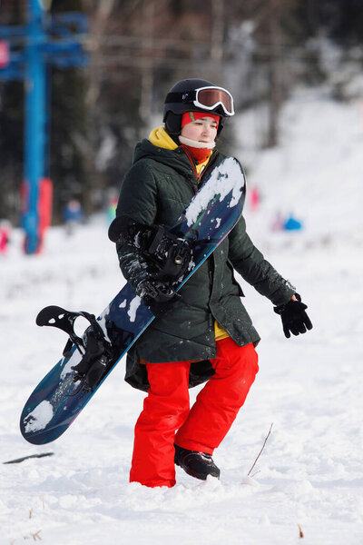 Woman snowboarder walks on the snowy mountain. She is wearing a mask, helmet, glasses and a red pants. Healthy lifestyle. The concept of sport. Selective focus.