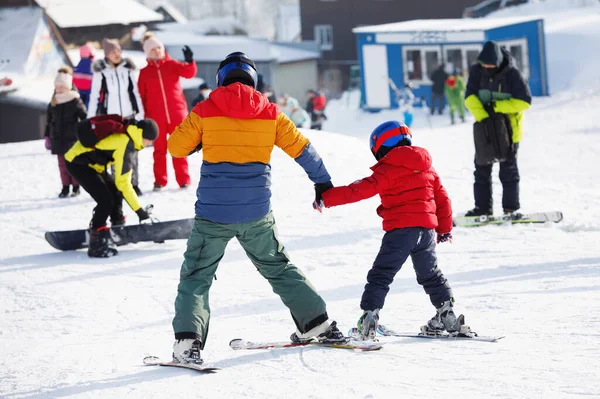Skiers glide down the slope of a snowy mountain at a natural resort. Adult holds a child by the hand. Ski equipment: pants and warm jacket, hard hat. Selective focus. — Stock Image Skiers Glide Slope Snowy Mountain Natural Resort Adult Holds Child Royalty Free Stock Images