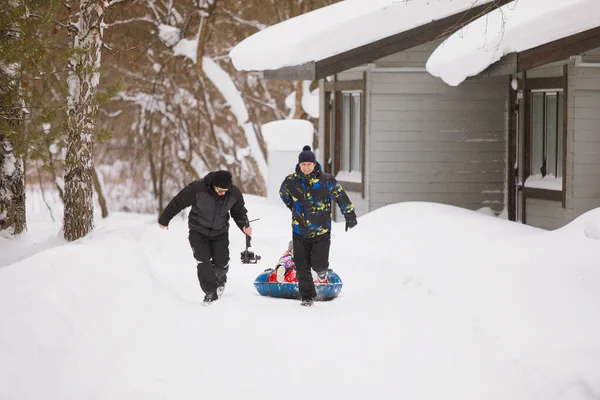 Video filming with the Steadicam in motion. Man rides his daughter in a tubing through the snow.