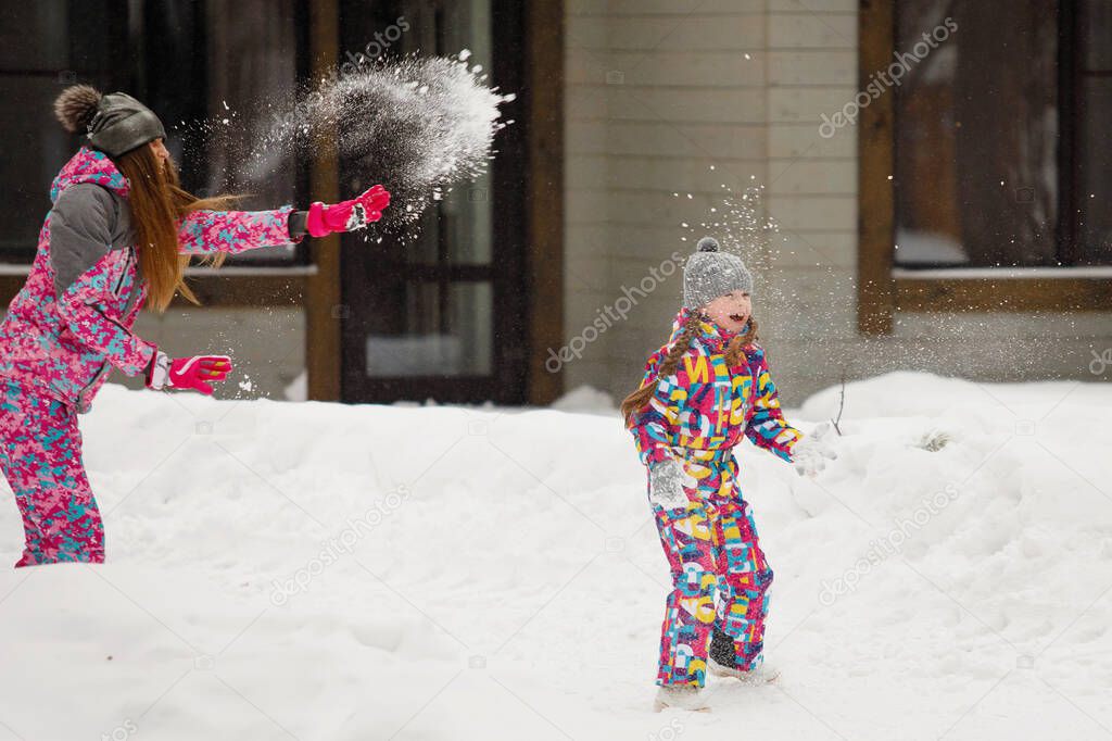 Mom and daughter throw snowballs in a winter snow park. Selective focus, blurred background.