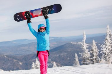 Snowboardcu panoyu yukarıda tutuyor. Kapüşonlu mavi ceket, örgü şapka, kayak gözlüğü. Sağlıklı bir yaşam tarzı. Spor konsepti. Seçici odak.